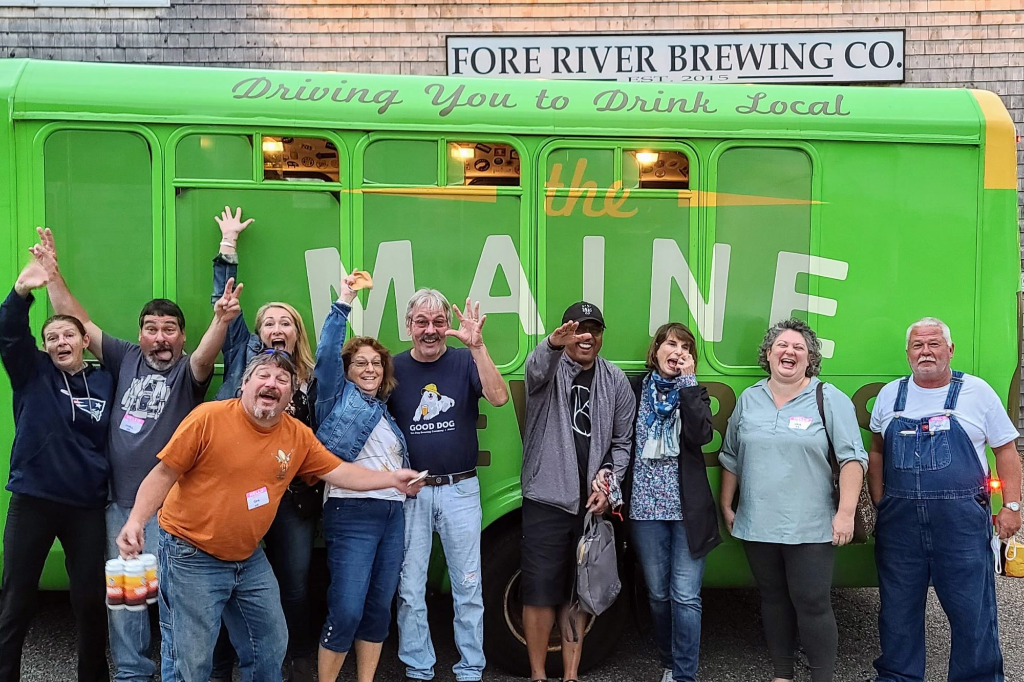 Group of people posing excitedly in front of a green bus with 'Maine' on it.