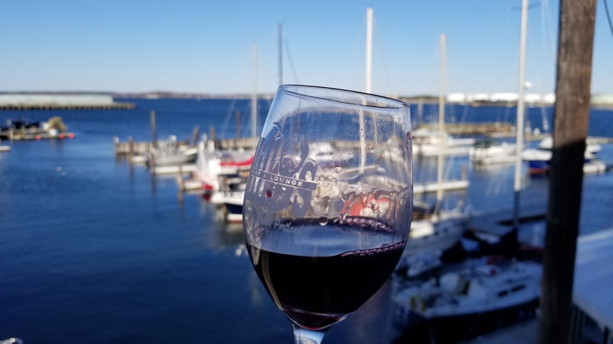 Glass of red wine in focus with a marina and boats in the background.