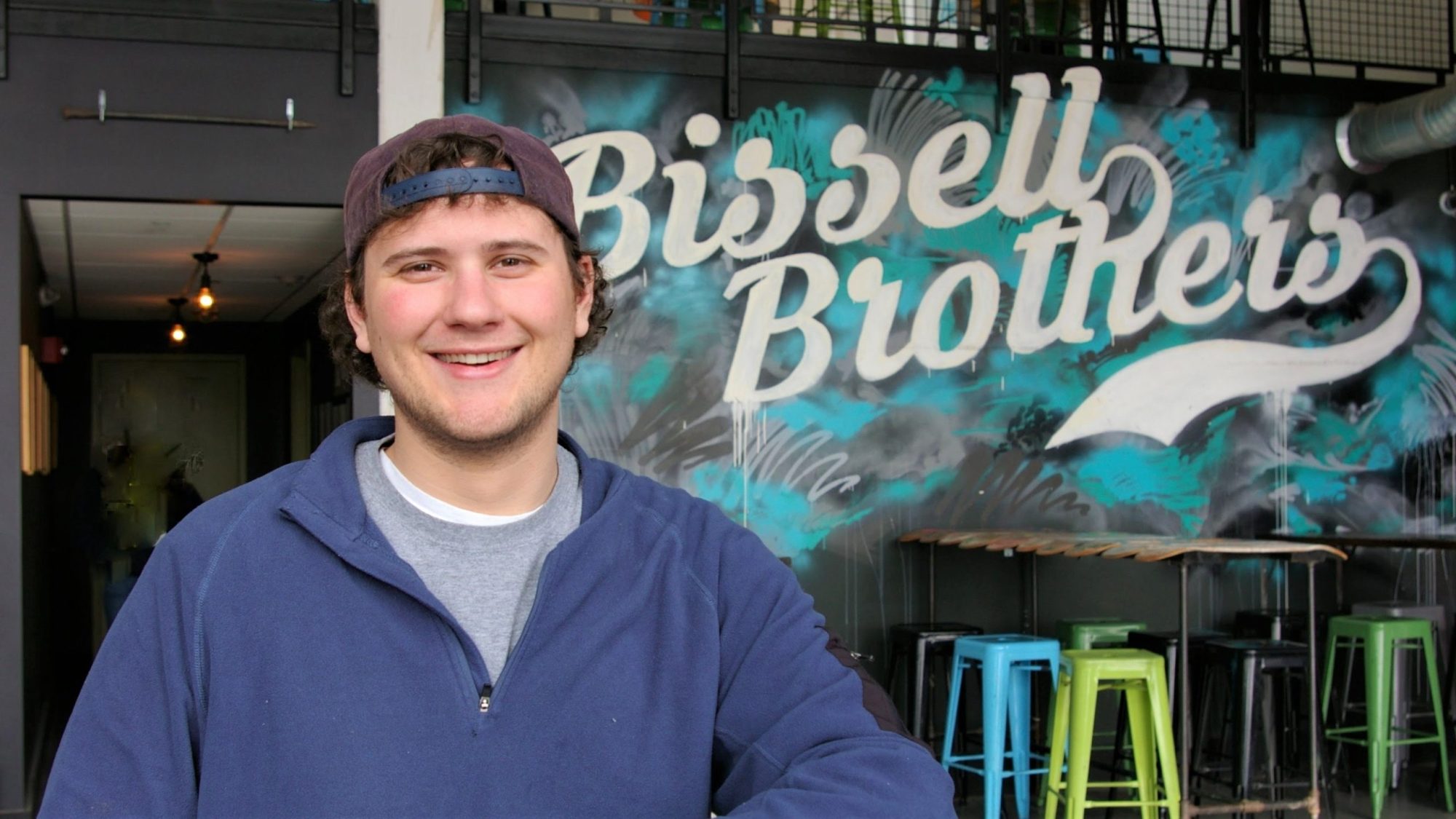Person smiling in front of Bissell Brothers mural with colorful stools.