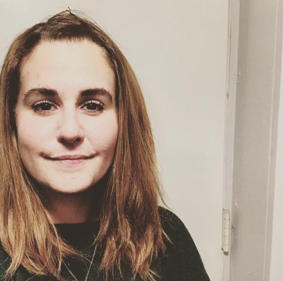 Person with medium-length brown hair and a neutral expression in a well-lit room.