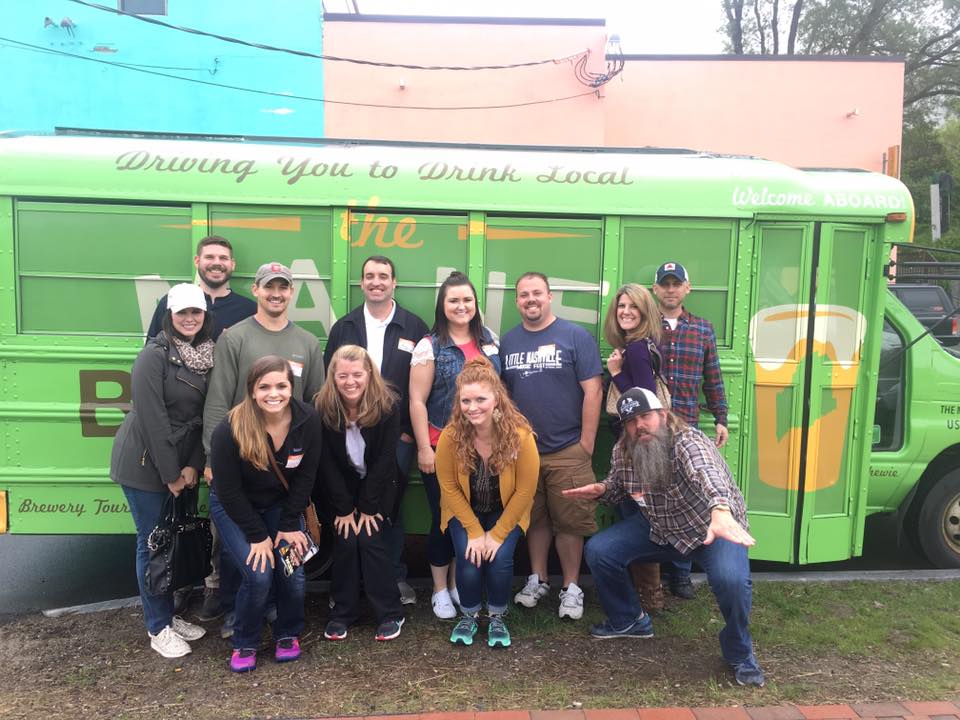 Group of people posing in front of a green brewery tour bus.