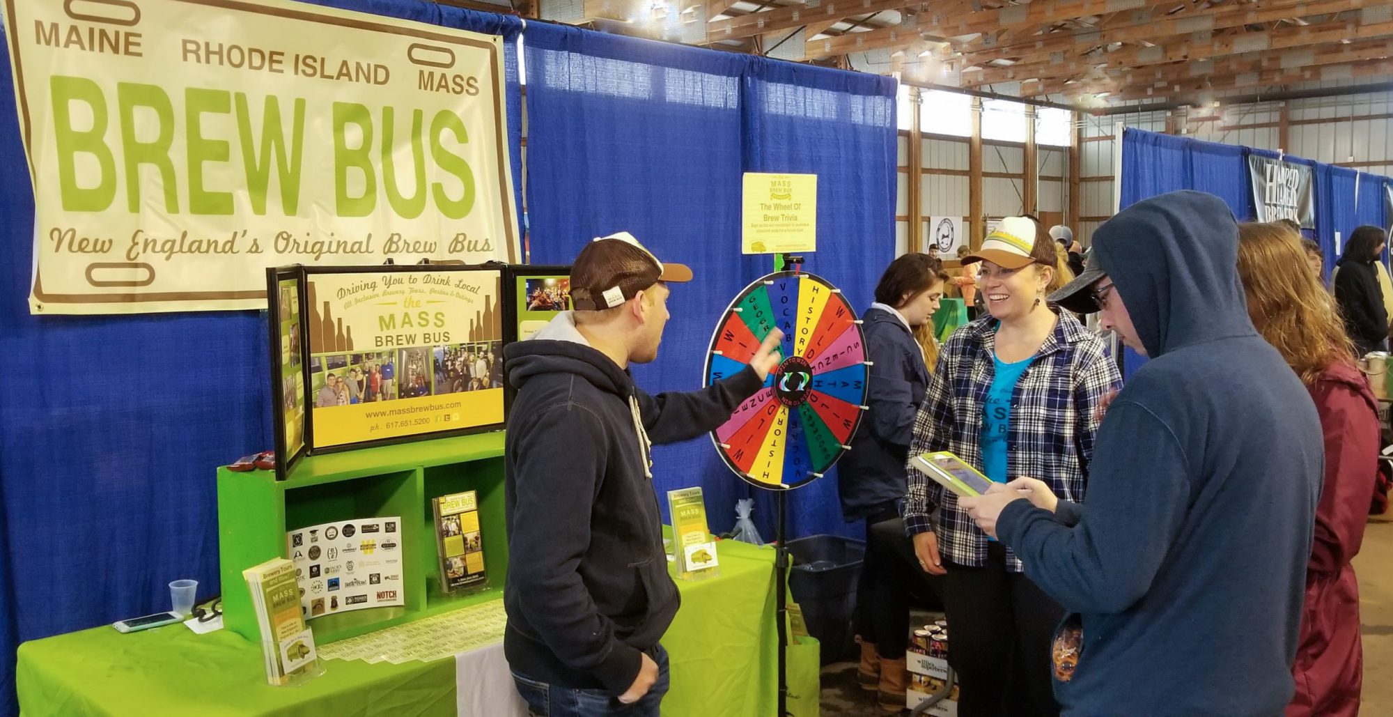 People at a 'Brew Bus' booth with a prize wheel at a fair.