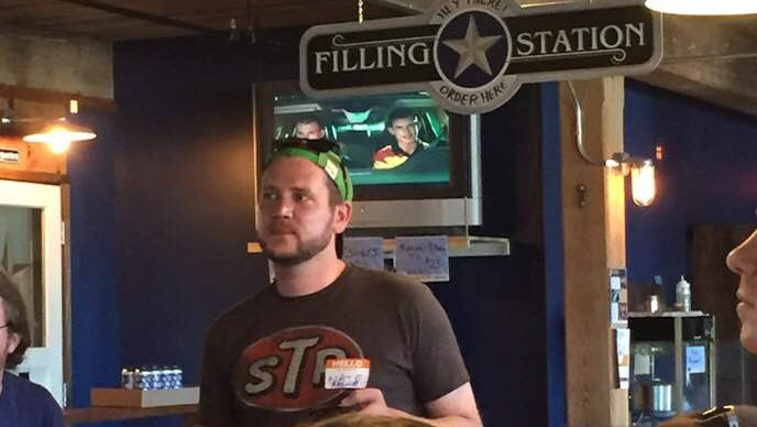 Man in cap at Filling Station, TV in background, blue walls.