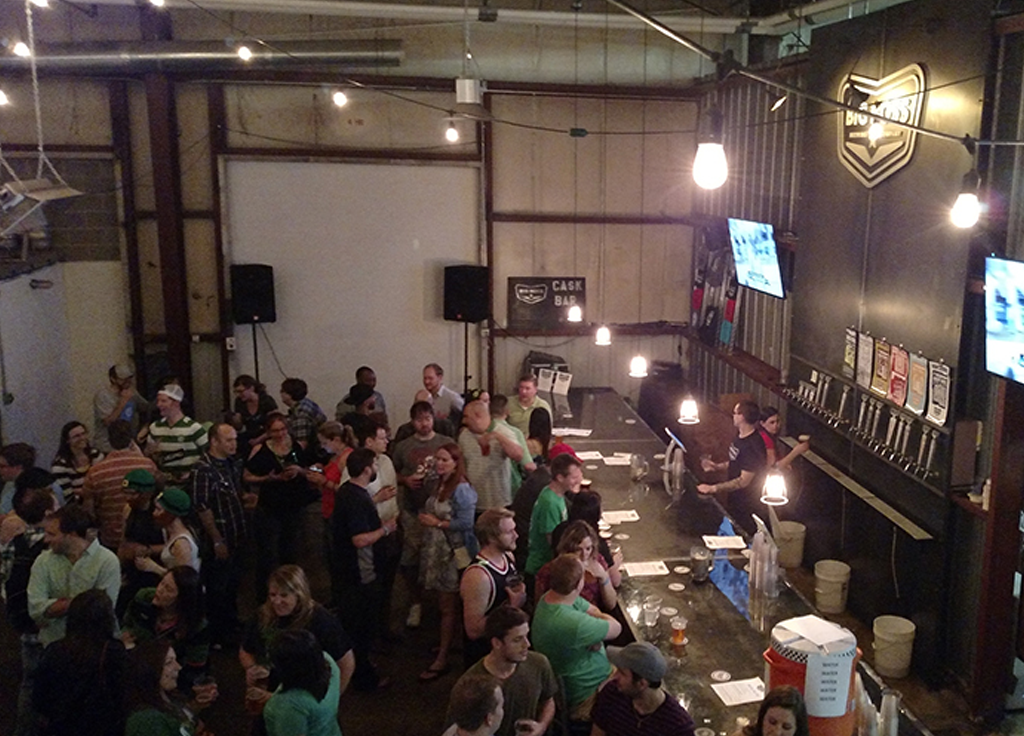 Crowded brewery bar with people socializing and ordering drinks.