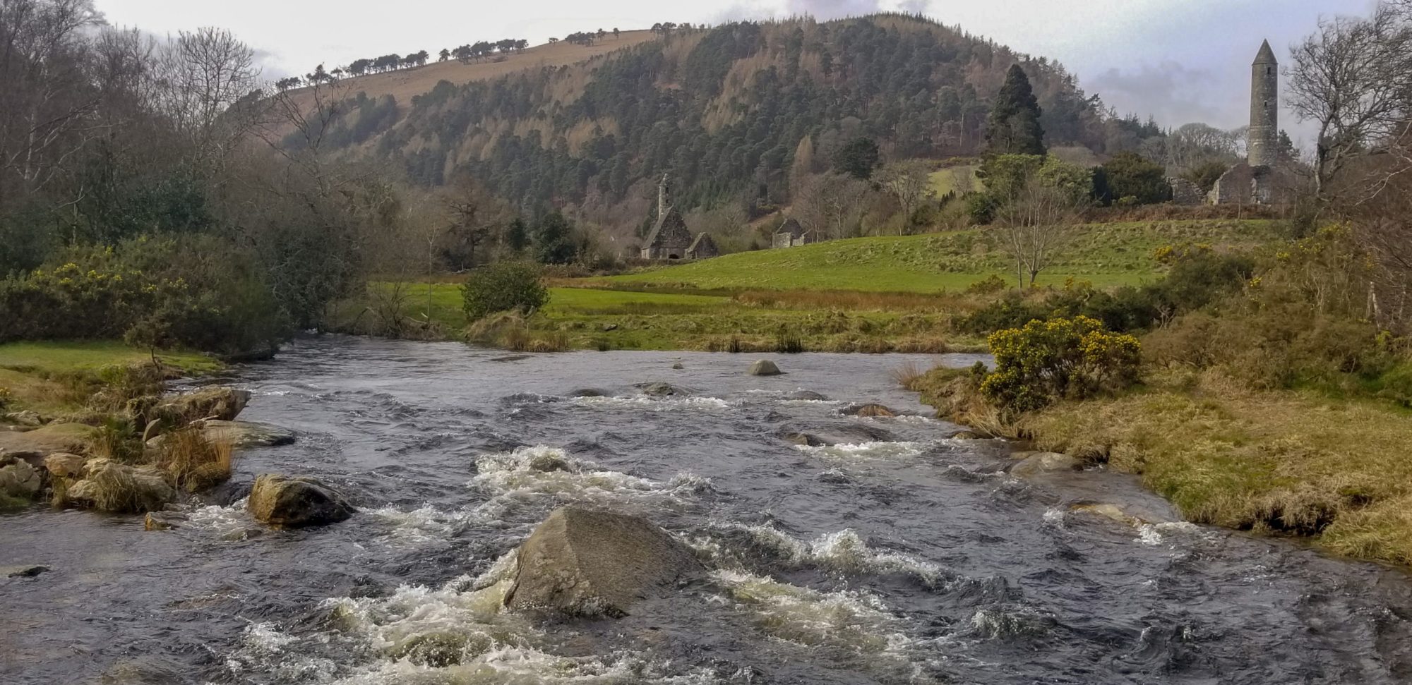 River flowing through grassy landscape with hills and a stone tower in the background.