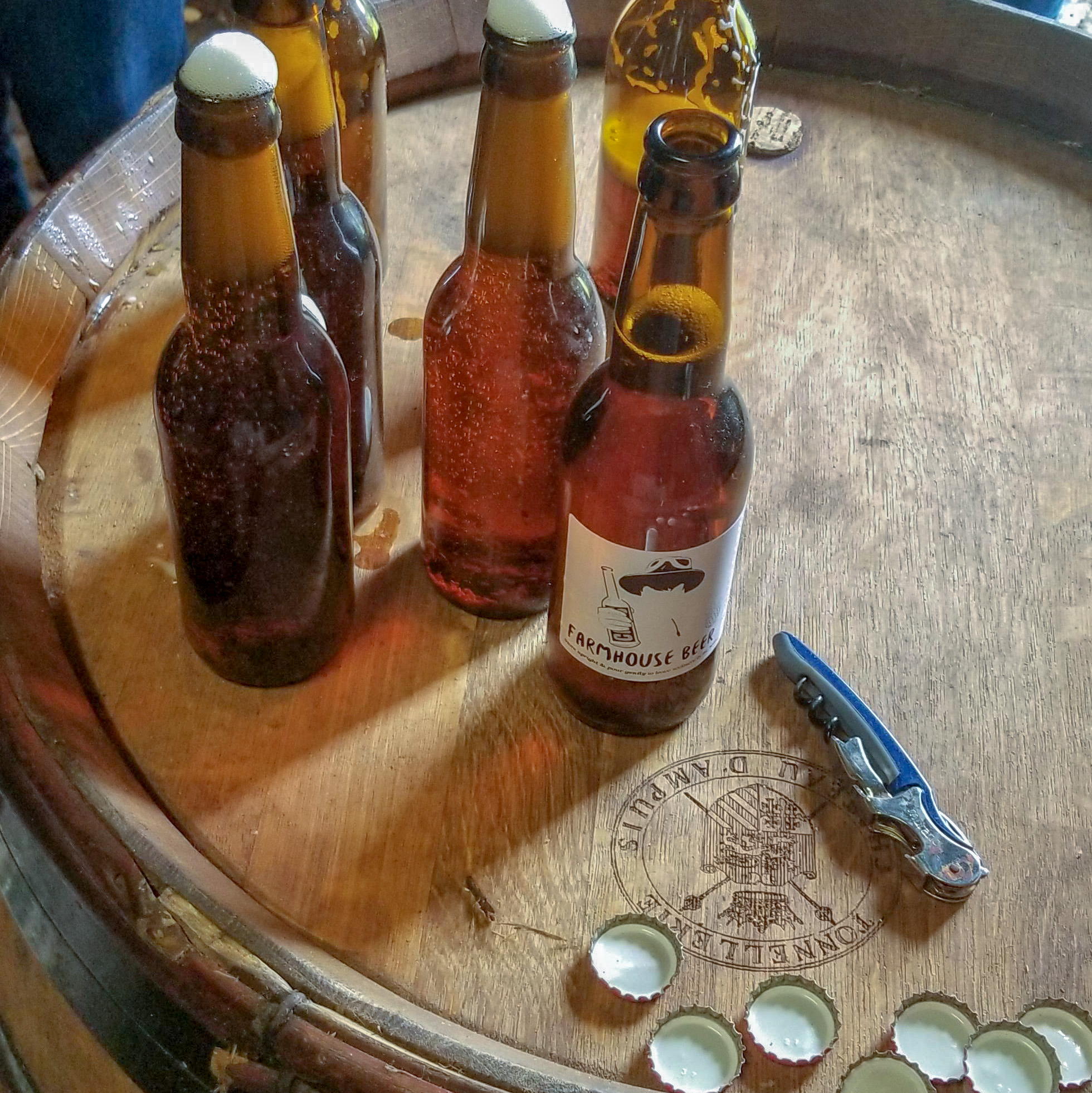 Bottles of beer, corkscrew, and caps on a wooden barrel surface.