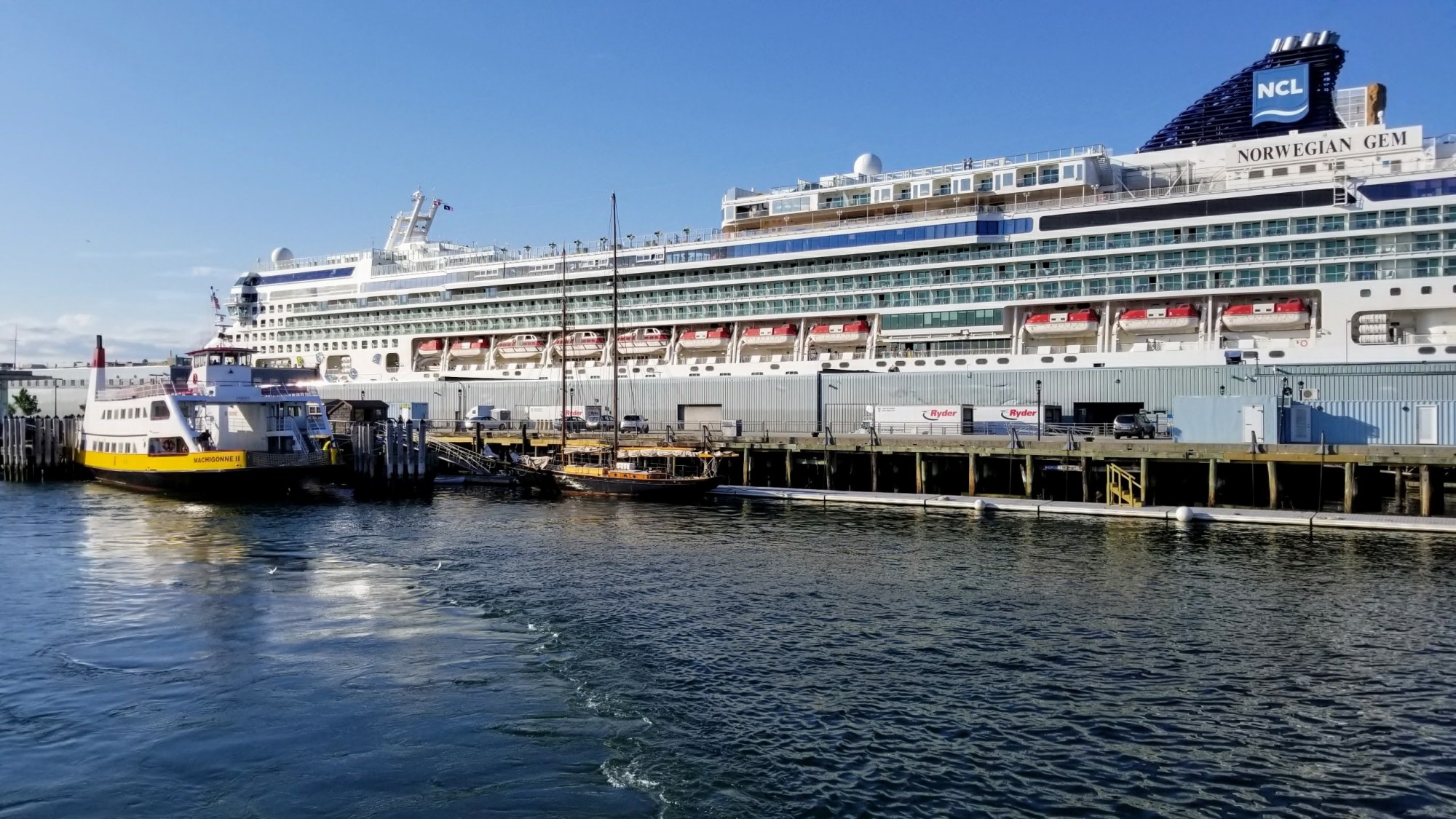 Cruise ship and smaller boats docked at a pier on a sunny day.