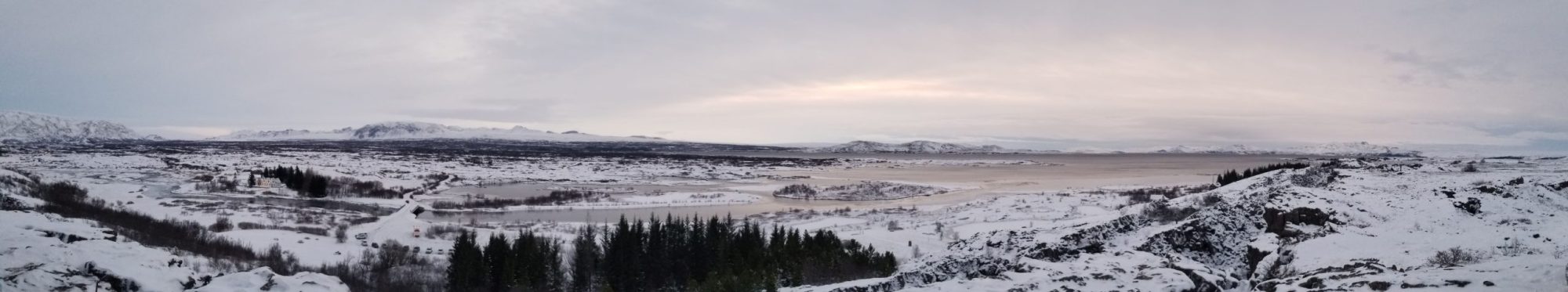 Panoramic view of a snowy landscape with trees and distant mountains under a cloudy sky.