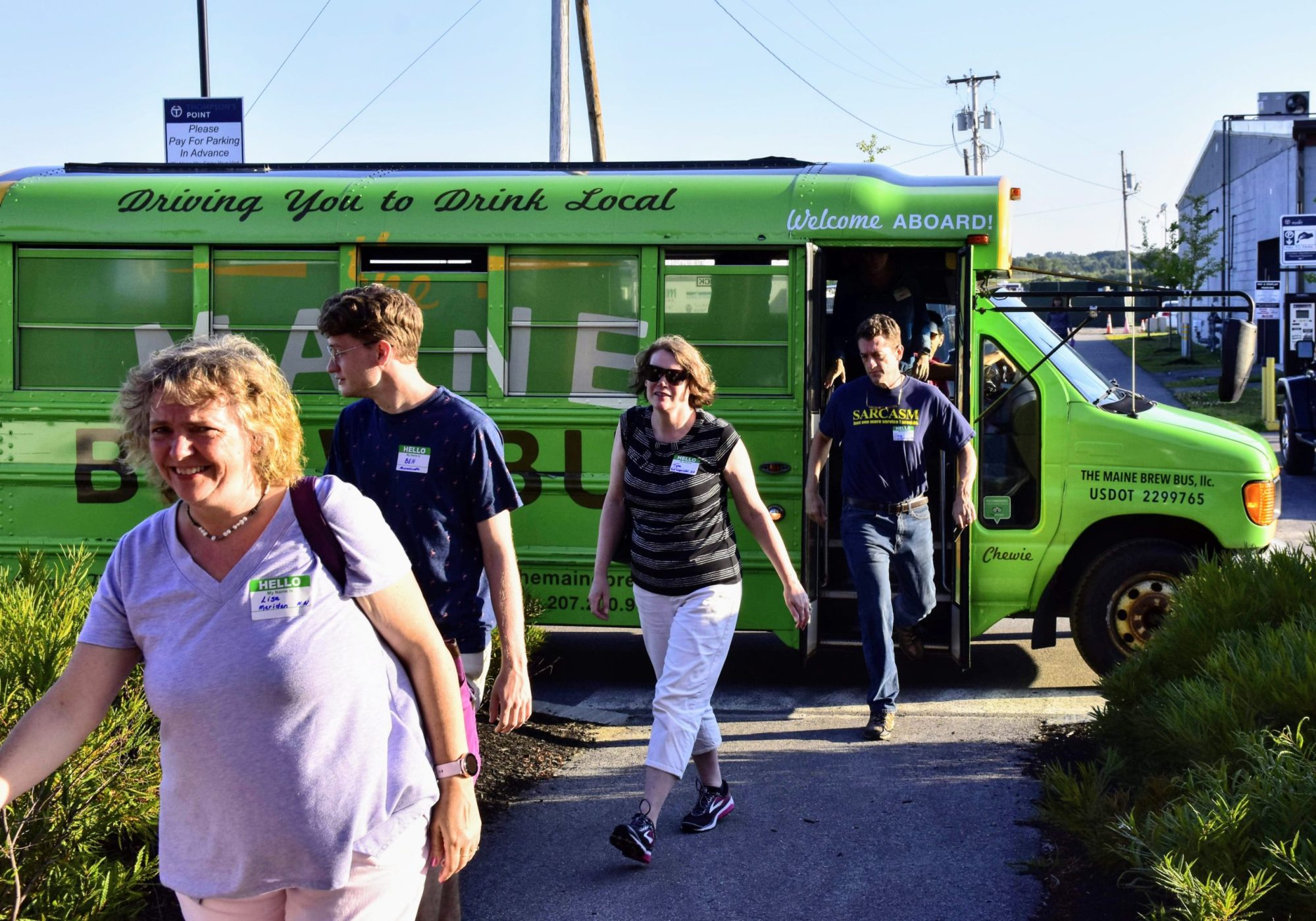 People exiting a green bus labeled 'Maine Brew Bus' parked in a sunny outdoor area.