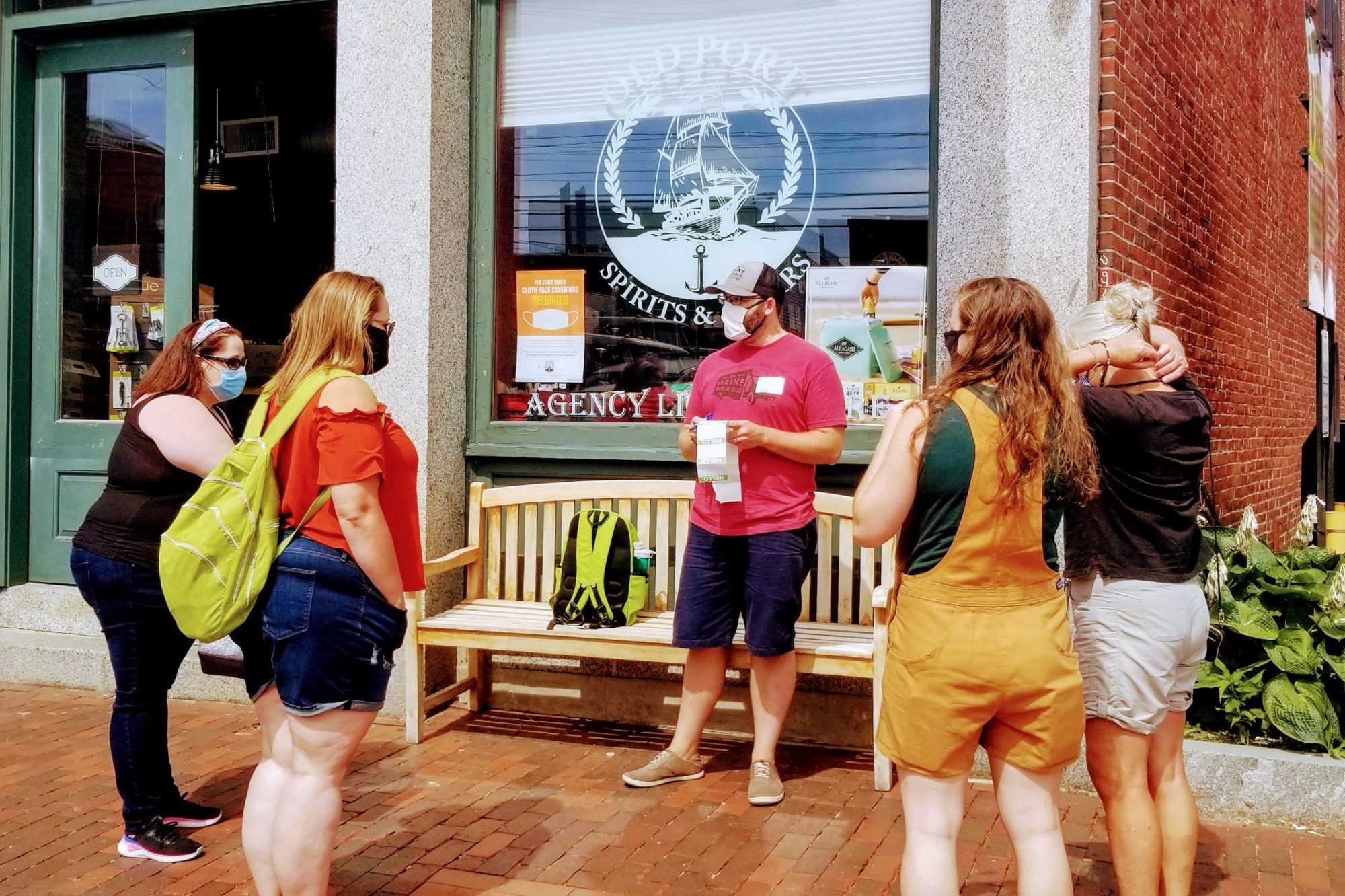 A group of people with masks gather outside a store with a nautical logo.