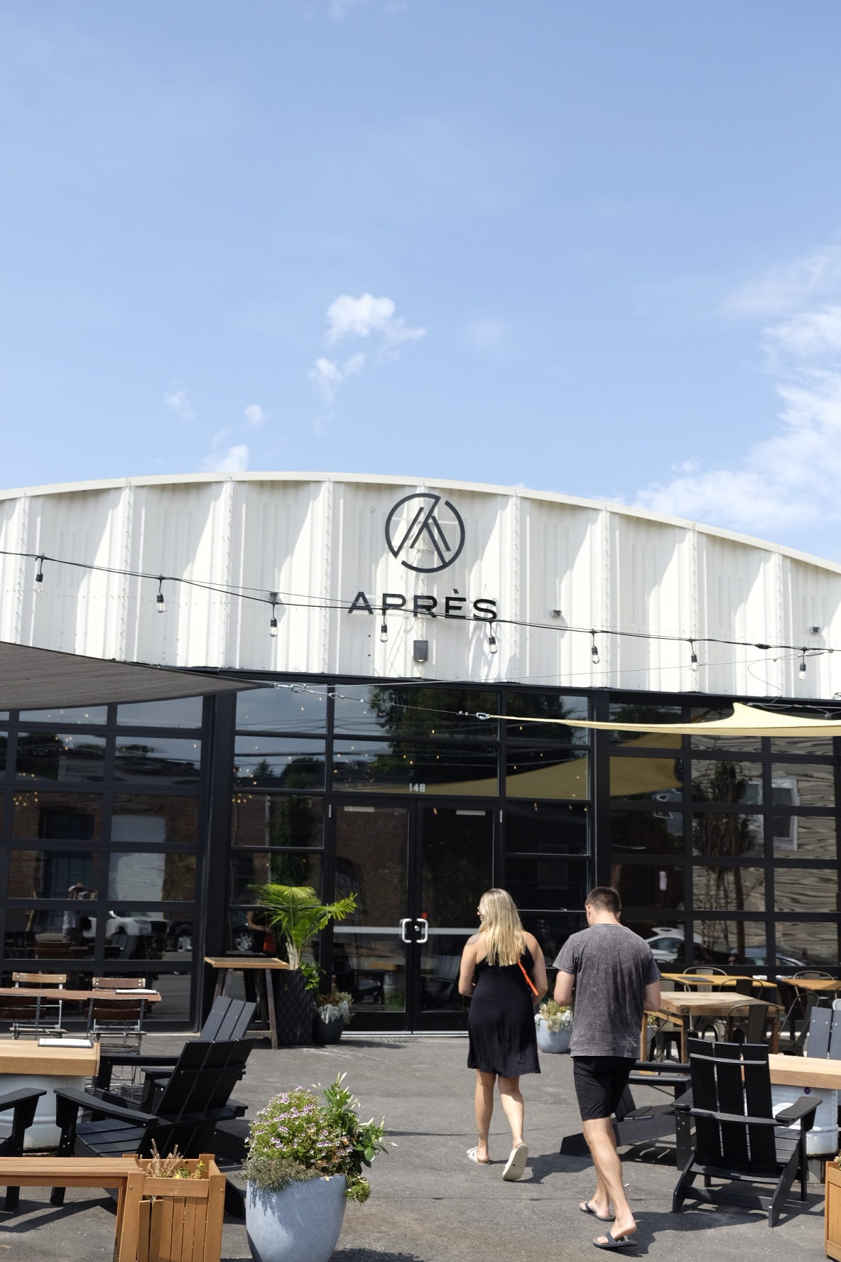 Two people walking towards a building with 'APRÈS' sign, under a clear blue sky.