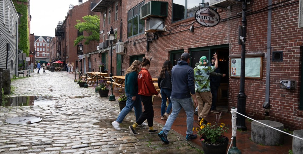 Group entering a rustic brick pub named Gritty's on a cobblestone street.