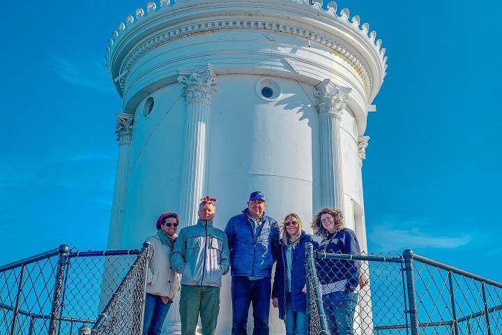 Five people stand in front of a white lighthouse with a blue sky.