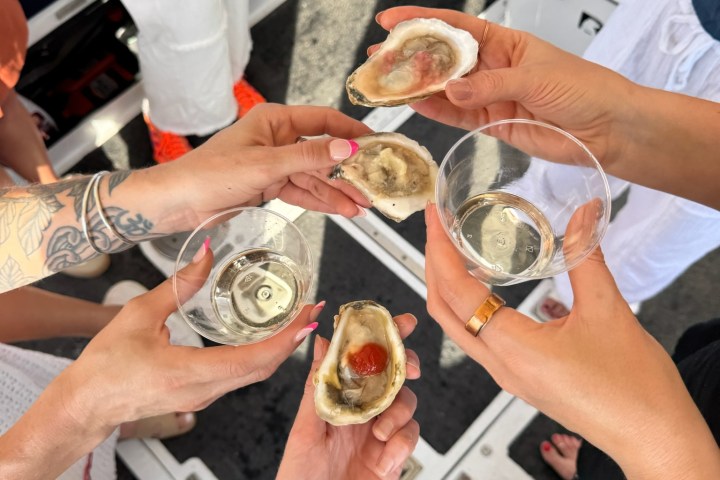 People holding oysters and wine glasses in a boat setting.