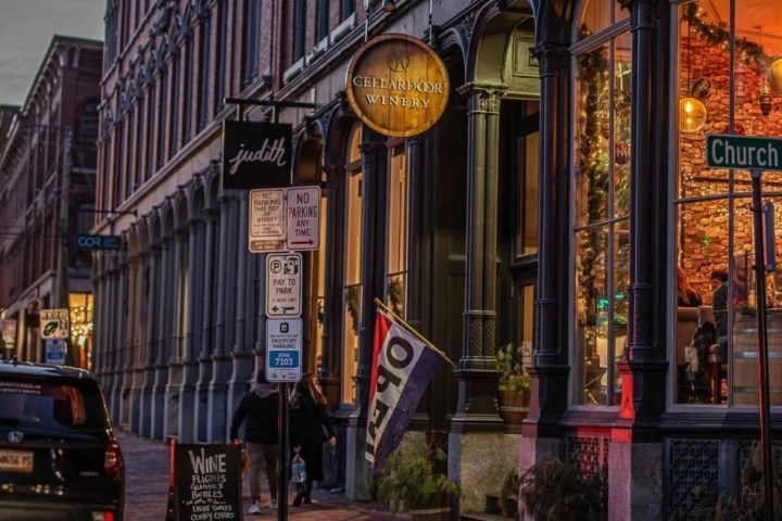 Night street view of a winery at corner of Church St, illuminated with people inside and a parked car outside.