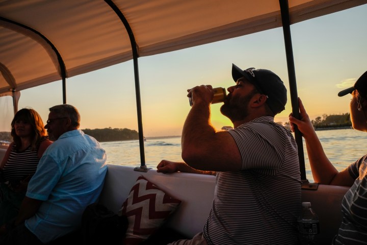 People on a boat at sunset, one man drinking from a can.