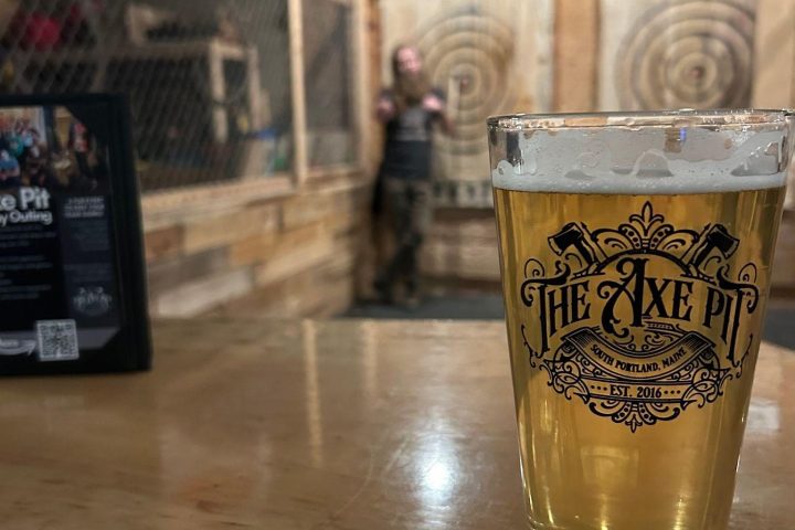 Glass of beer on table, axe throwing targets blurred in background at 'The Axe Pit' venue.
