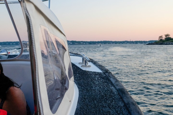 Boat with canopy on water with distant shoreline at sunset.