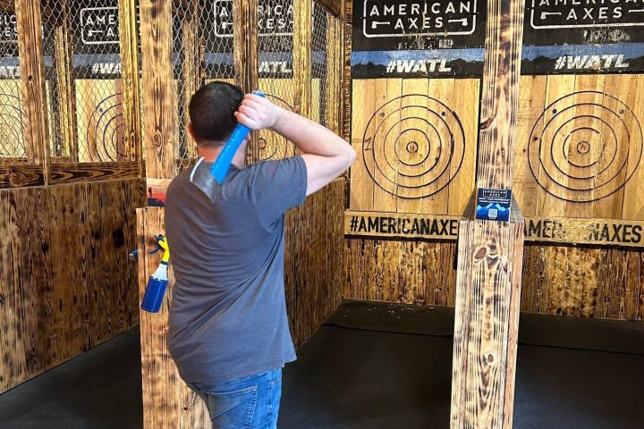 Person in blue jeans throwing an axe at a wooden target in an indoor range.