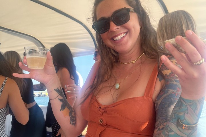 Woman in orange dress with tattoos holding a drink and smiling on a boat.