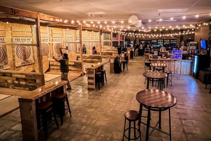 Indoor axe throwing venue with targets and tables, lit by string lights.