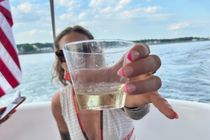 Person holding a beverage in a clear cup on a boat with a flag in the background.