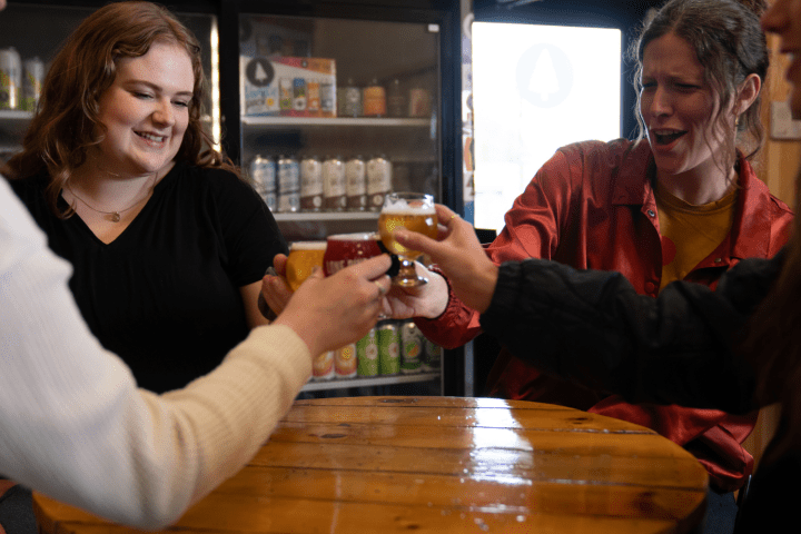 Group of people clinking glasses at a wooden table in a bar.