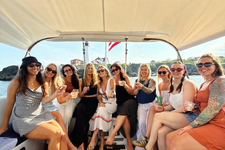 Group of women sitting on a boat under a canopy, smiling and holding drinks.
