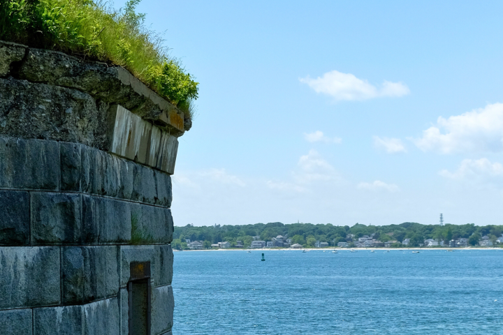 Stone wall by a calm blue sea with distant shoreline on a sunny day.