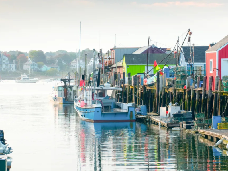Colorful harbor with boats, fishing huts, and lobster traps along a wooden pier on a calm water body.