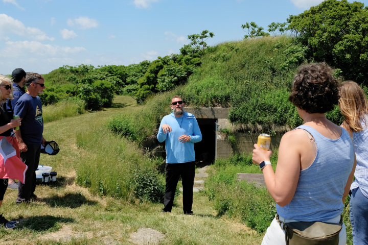 People listening to a guide outside a grass-covered bunker on a sunny day.