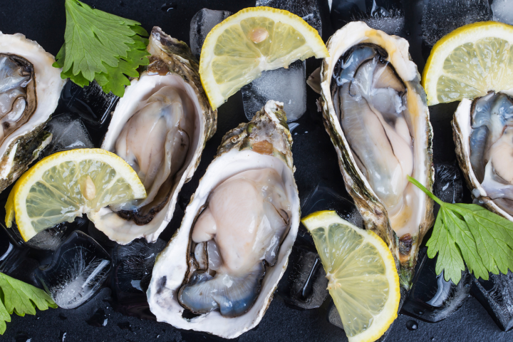 Fresh oysters on half shell with lemon slices and parsley on ice.