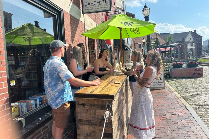 People gathered at an outdoor bar with a green umbrella on a sunny day.