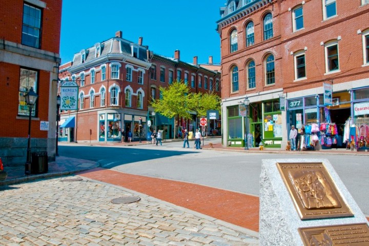 Street view with historic red brick buildings and a stone plaque on a sunny day.