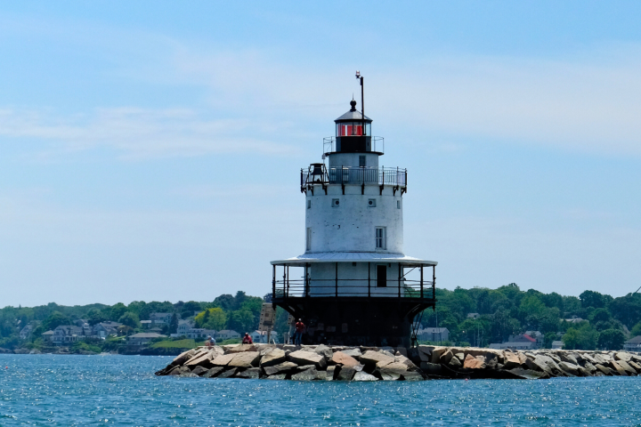 A lighthouse on a rocky pier surrounded by water under a clear blue sky.