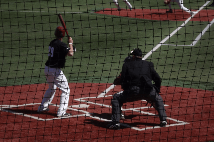 Baseball game with batter, catcher, and umpire at home plate, seen through a net.