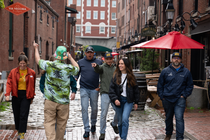 Group of people walking through a brick alley with a red umbrella overhead.