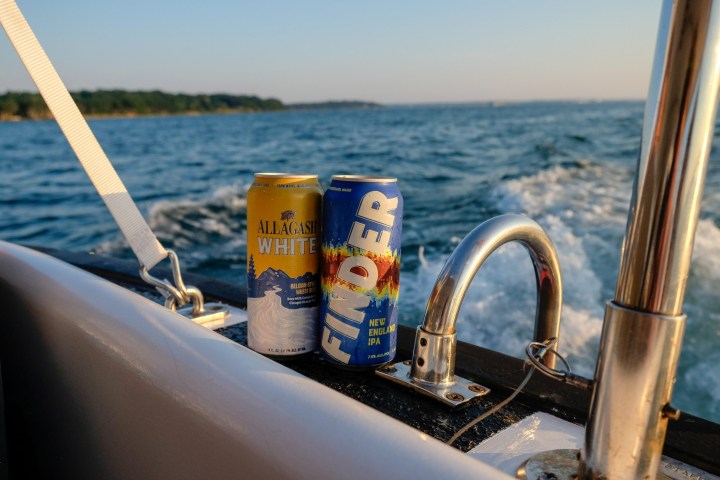 Two beer cans on a boat railing with ocean and sky in the background.