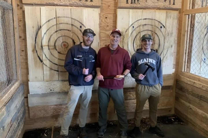 Three people holding axes in front of wooden targets at an axe throwing venue.
