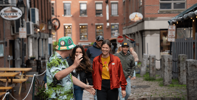 Group of people walking on a cobblestone street near brick buildings, with one person gesturing animatedly.