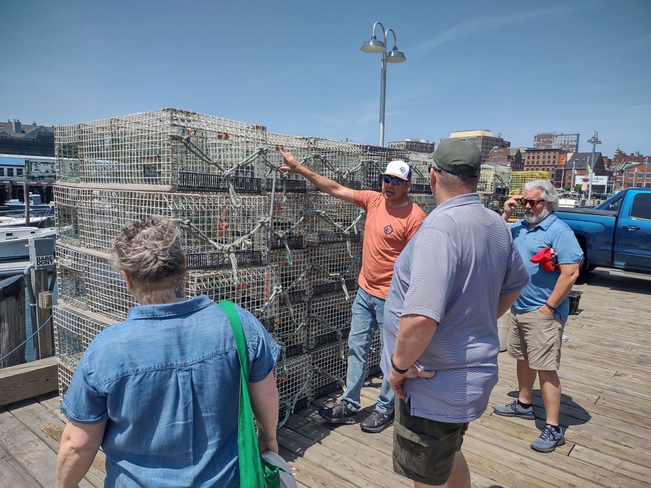 People standing near a stack of lobster traps on a dock under a clear sky.