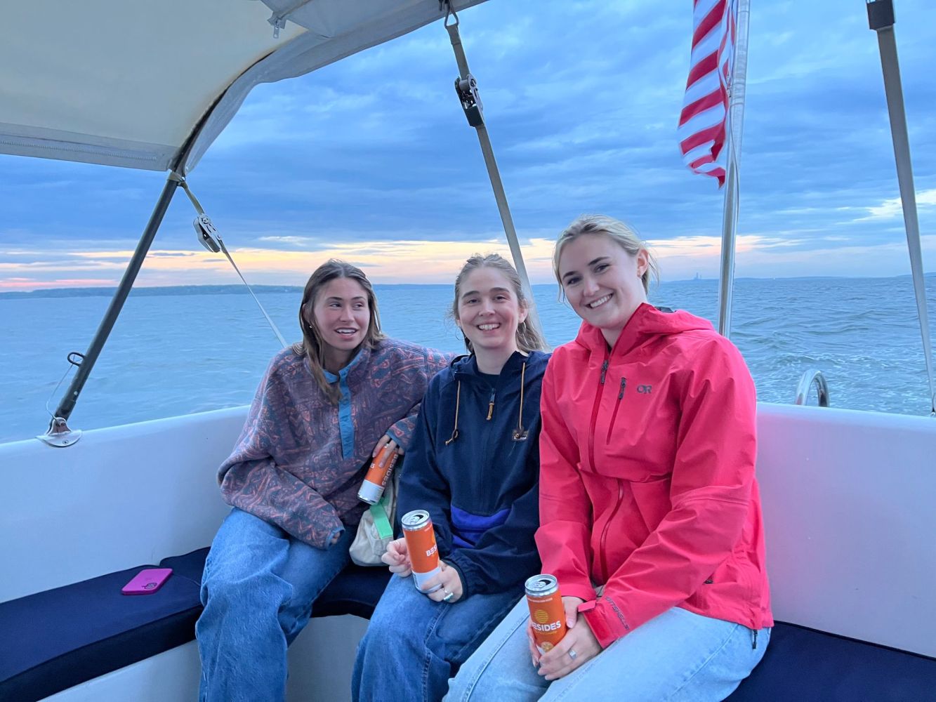 Three people sitting on a boat, smiling, with an American flag in the background.
