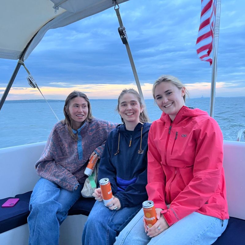 Three people sitting on a boat, smiling, with an American flag in the background.