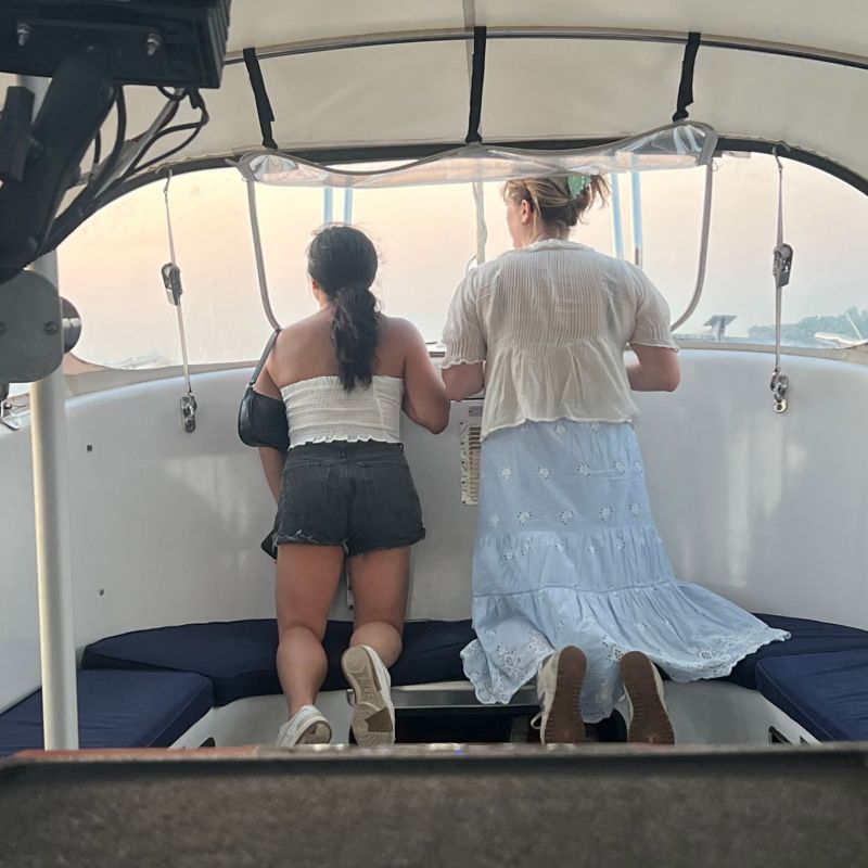 Two people kneeling on a boat bench, looking out the window.