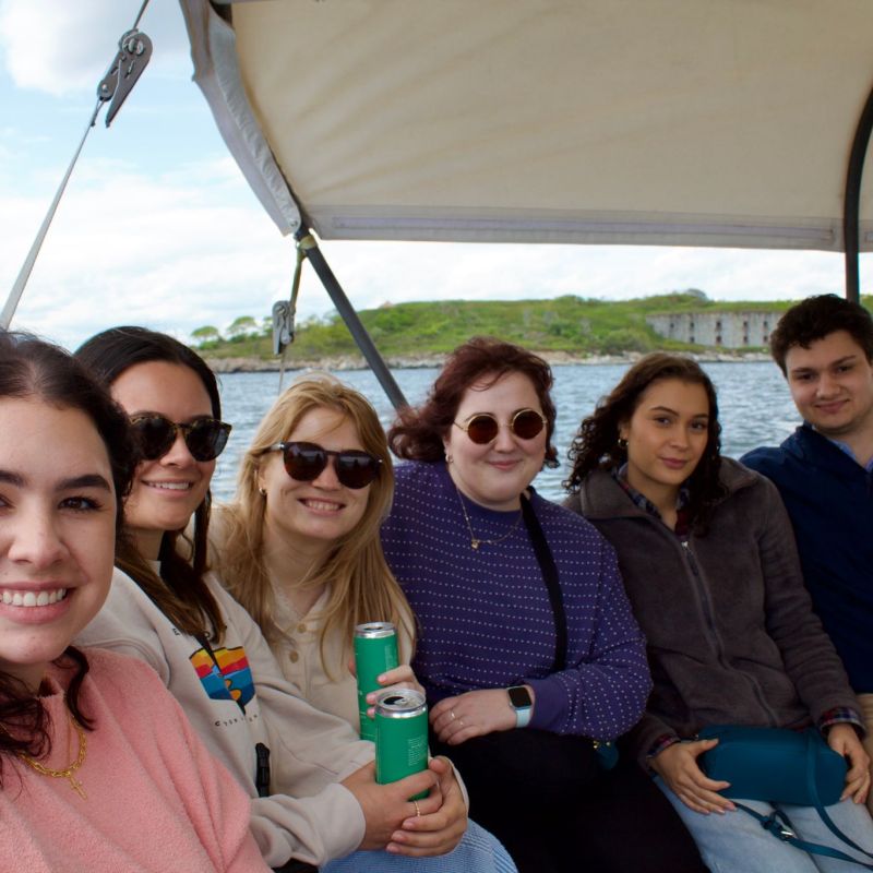 Group of six people smiling on a boat with water and greenery in background.