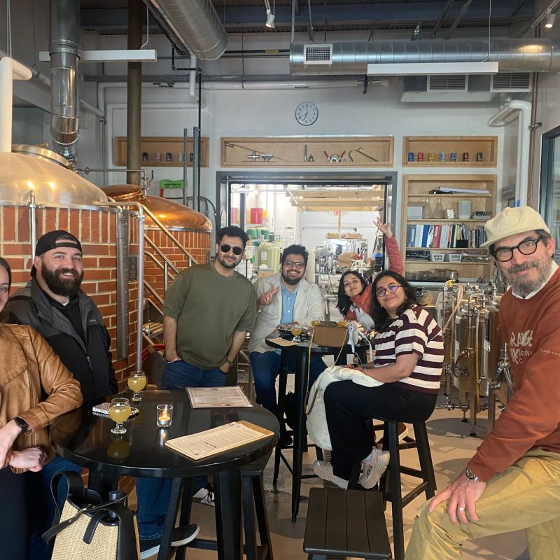 Group of people smiling and posing inside a brewery with tanks in the background.