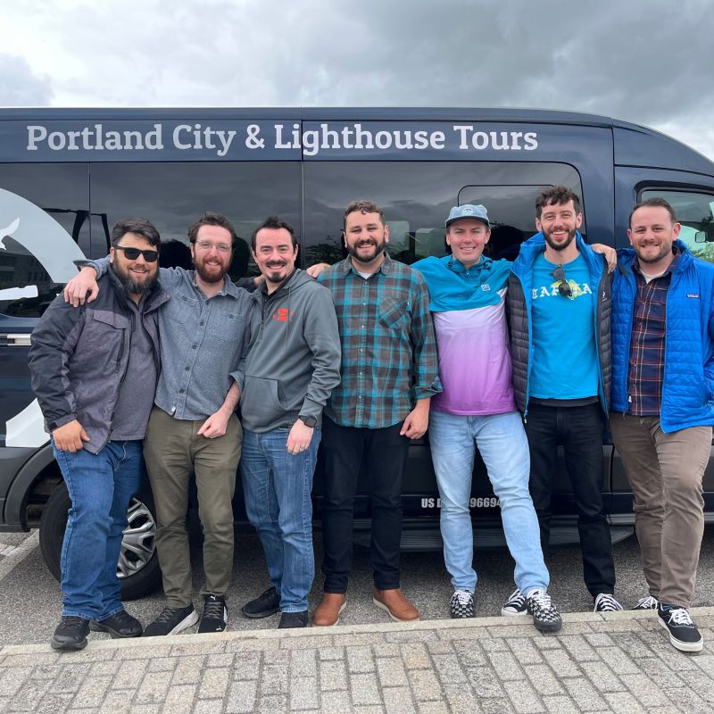 Seven people pose in front of a Portland City & Lighthouse Tours van on a cloudy day.