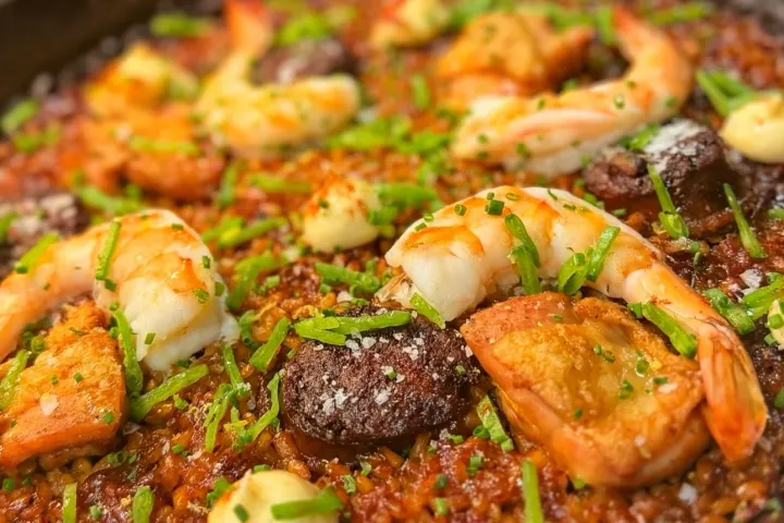 Paella dish with shrimp, chorizo, rice, and garnishes in a pan.