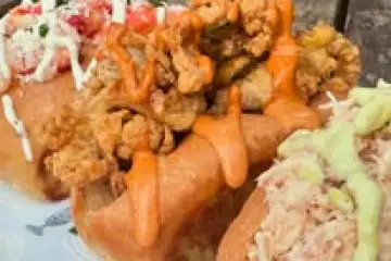 Three loaded sandwich rolls on a wooden table.