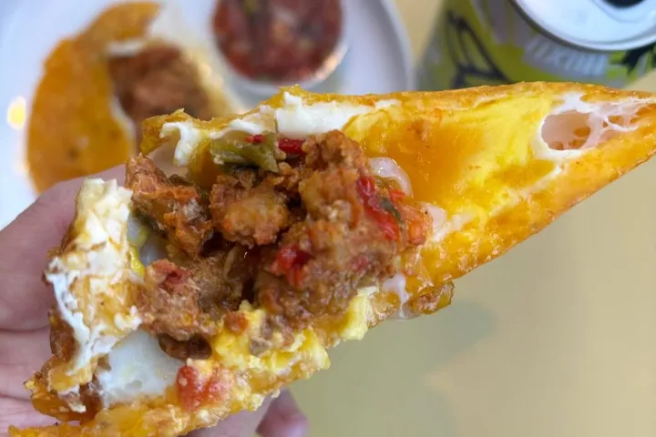 Hand holding a taco near a plate with salsa and a can on a yellow surface.